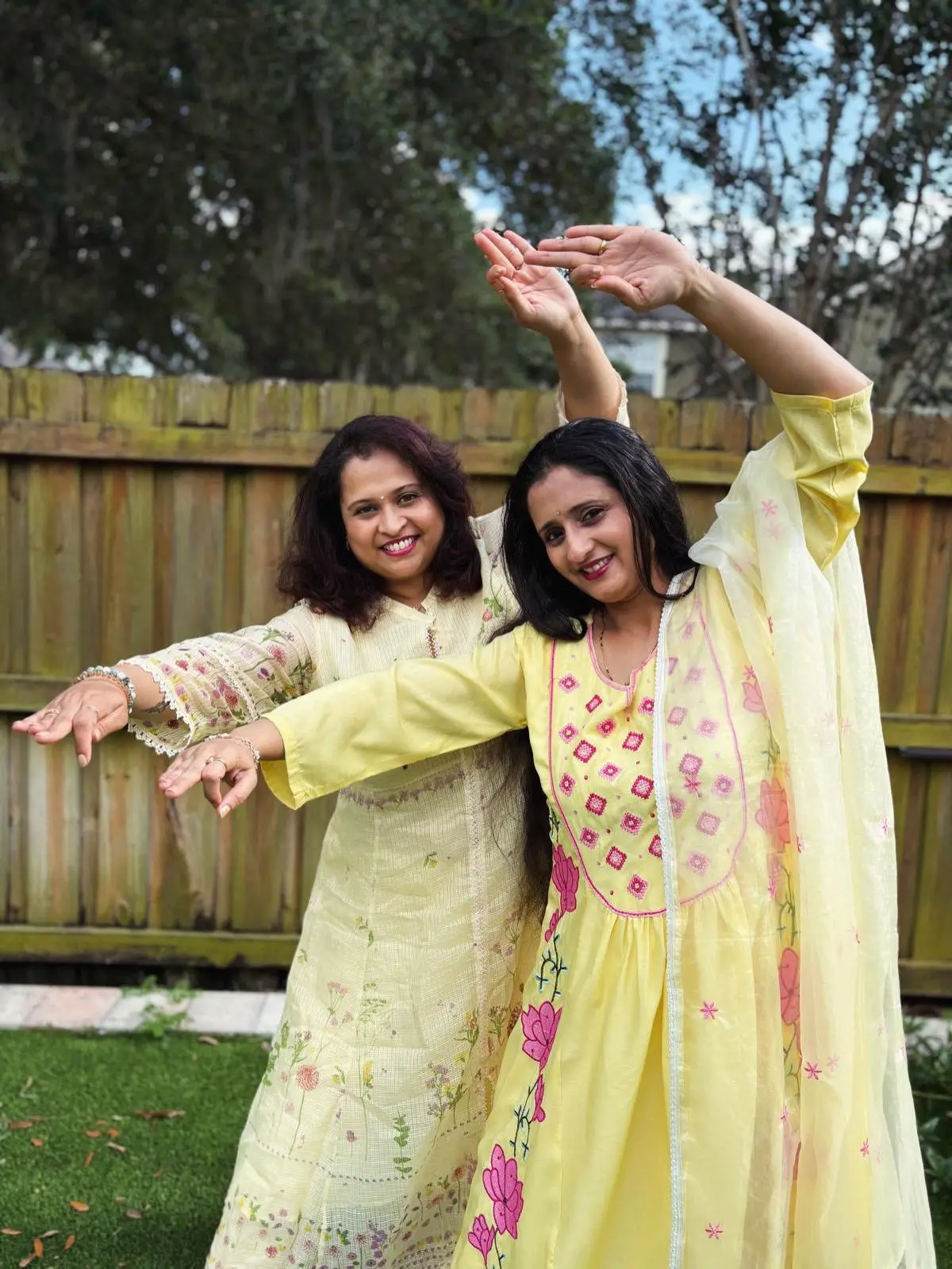 Ashwini Katre-Kulkarni and Manali Phadke mid-pose in yellow outfits, arms extended in a dance movement outdoors.
